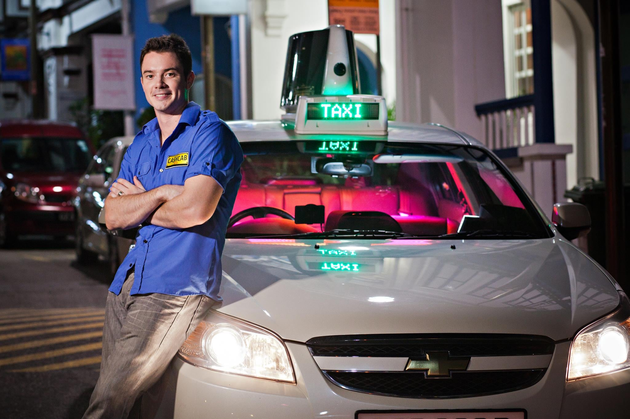 Cash Cab Asia host Oli Pettigrew standing beside the illuminated taxi