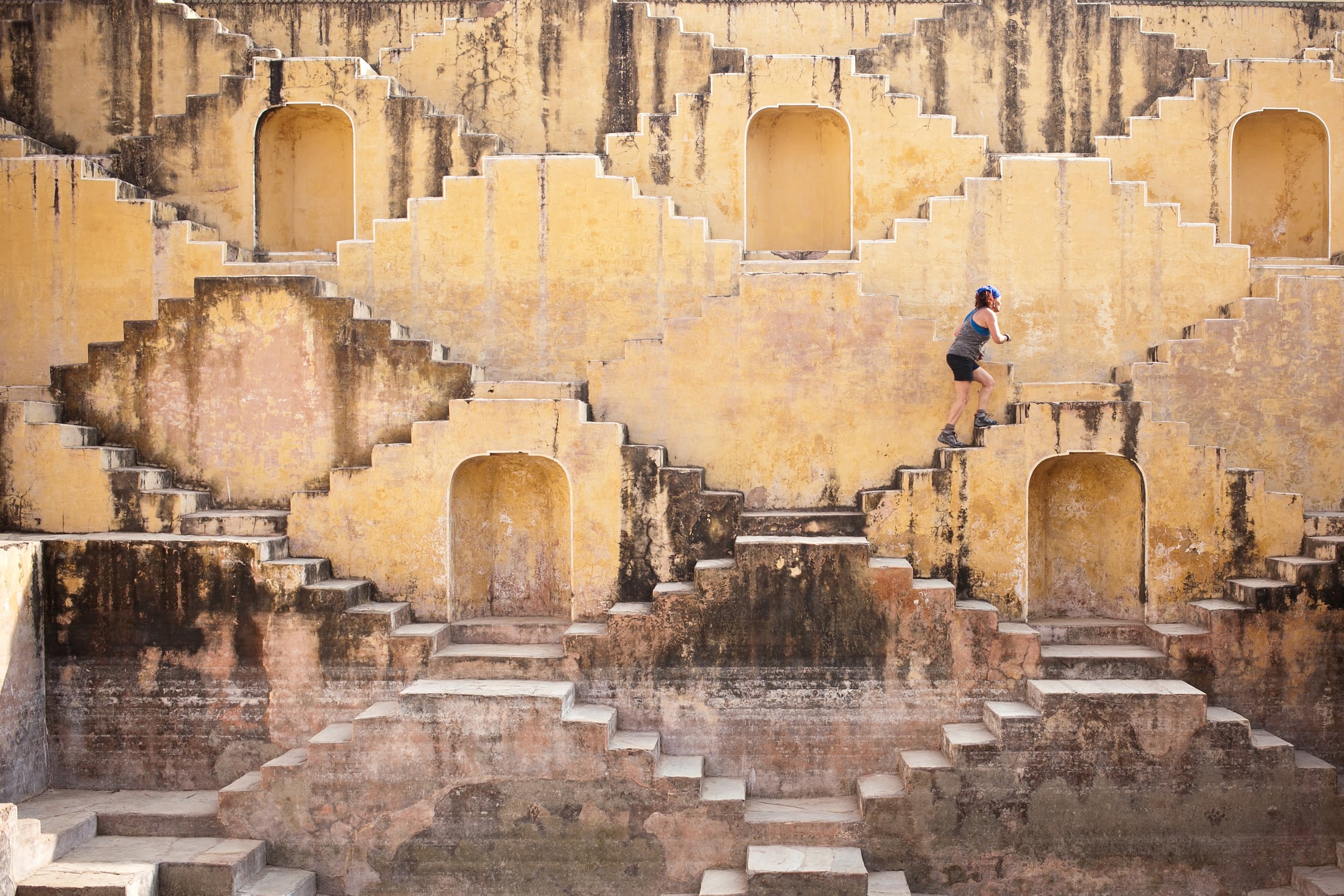 An Amazing Race contestant climbing through an architectural location